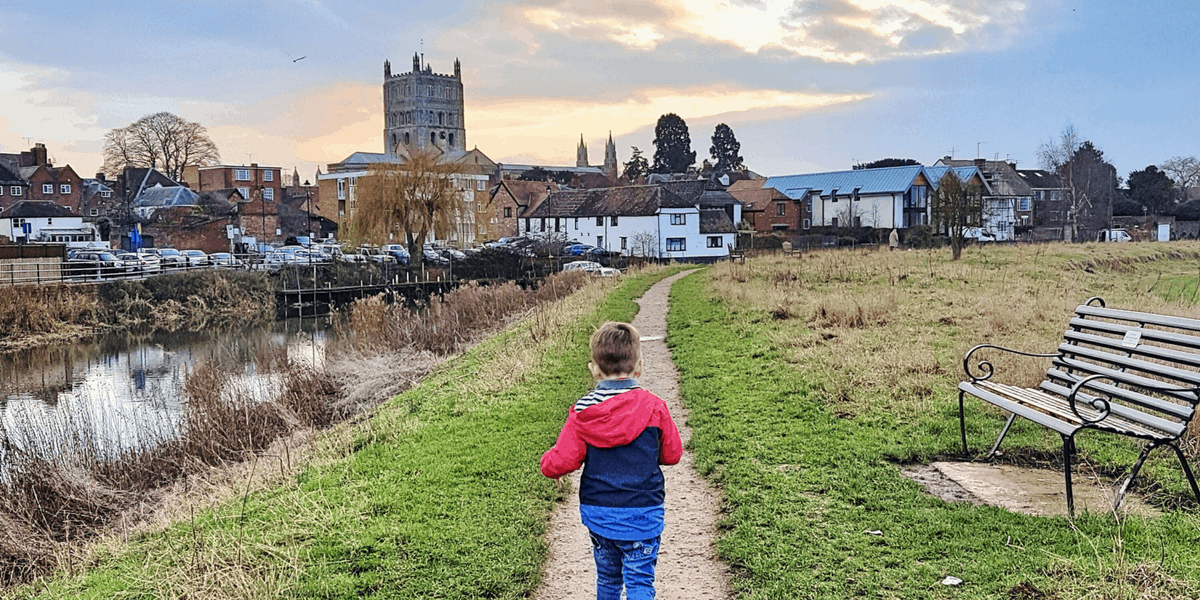 A young boy running along a river with a cathedral in the background.