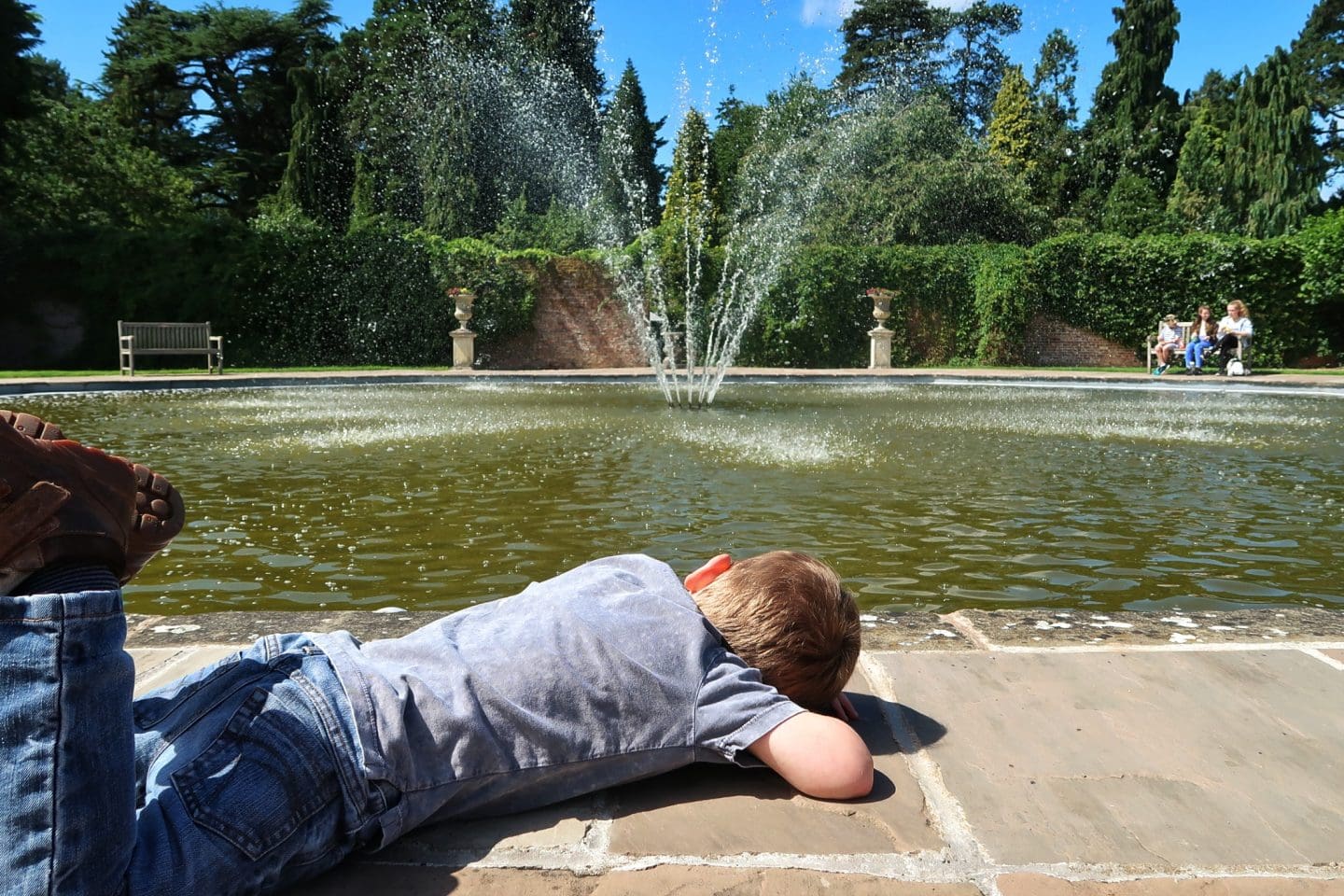A boy lying down to look at the fountain at Arley arboretum