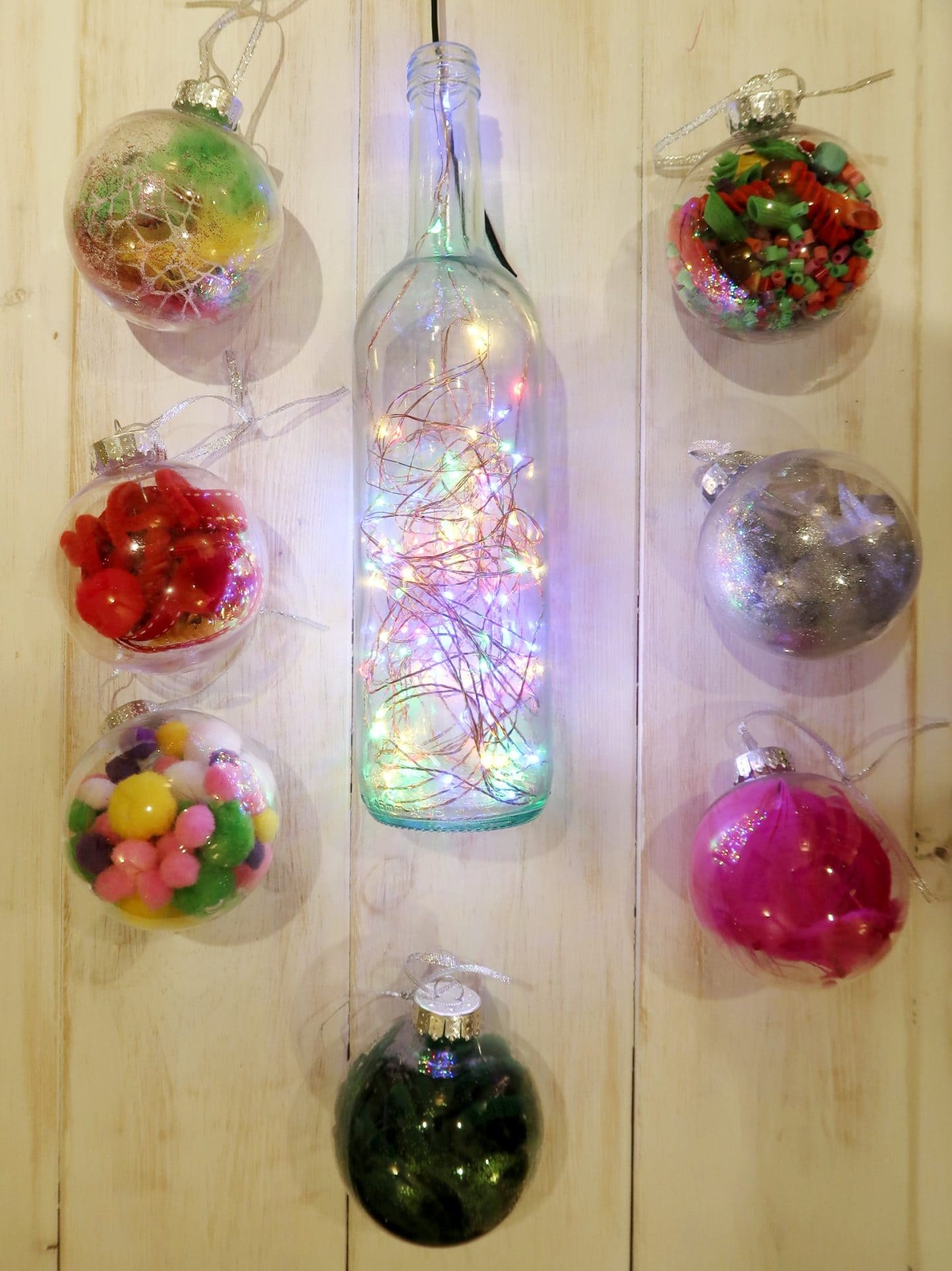 A selection of Christmas baubles with a wine bottle filled with coloured fairy light in the middle