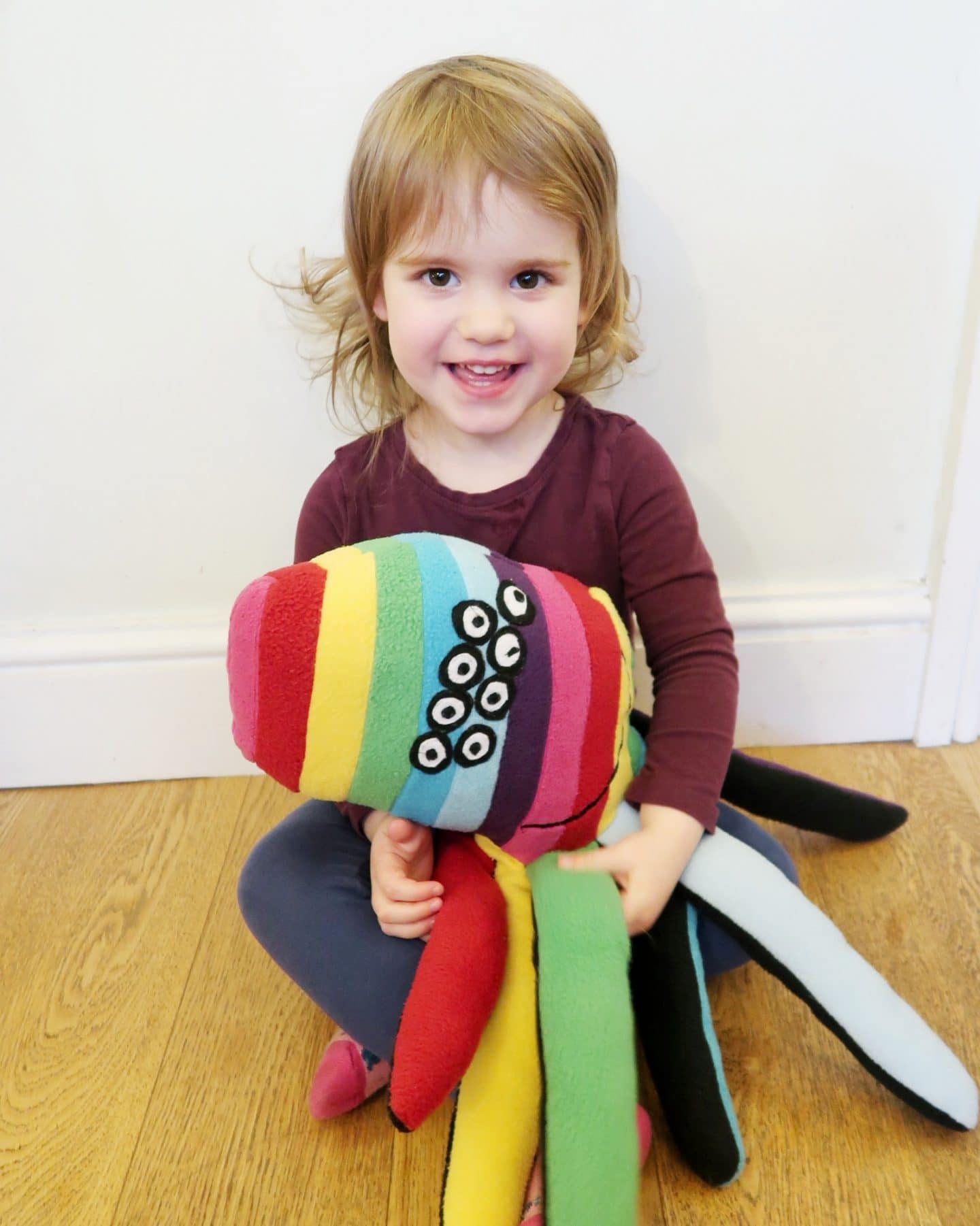 A small girl with a large rainbow spider soft toy