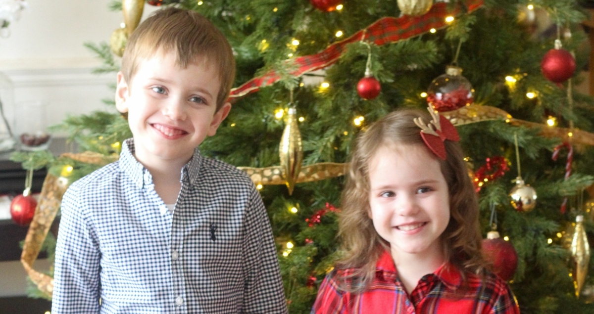 A small girl and boy holding in front of a christmas tree