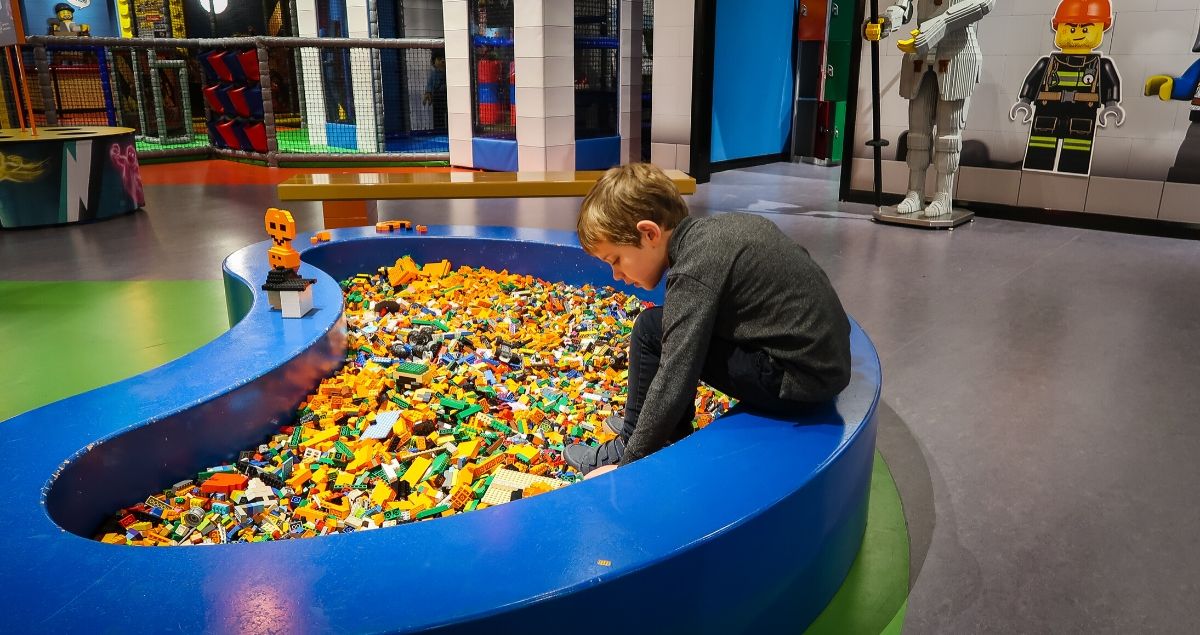 Boy beding over a large pit full of coloured lego