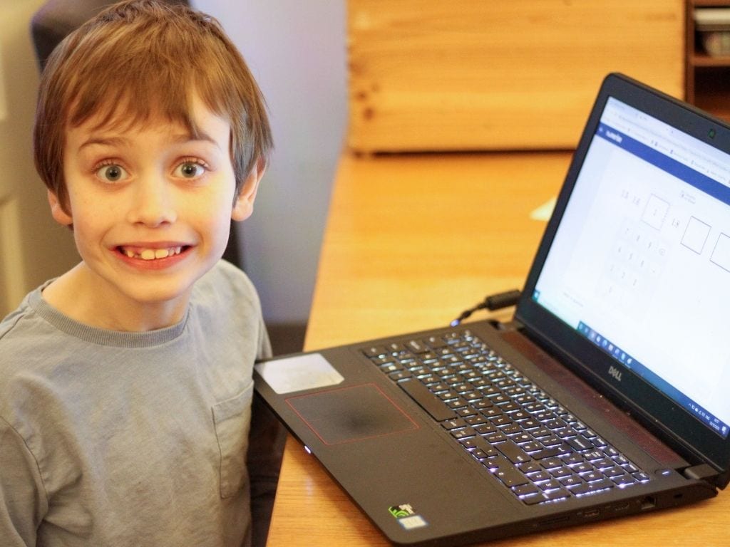 Very happy boy next to maths app on a laptop.