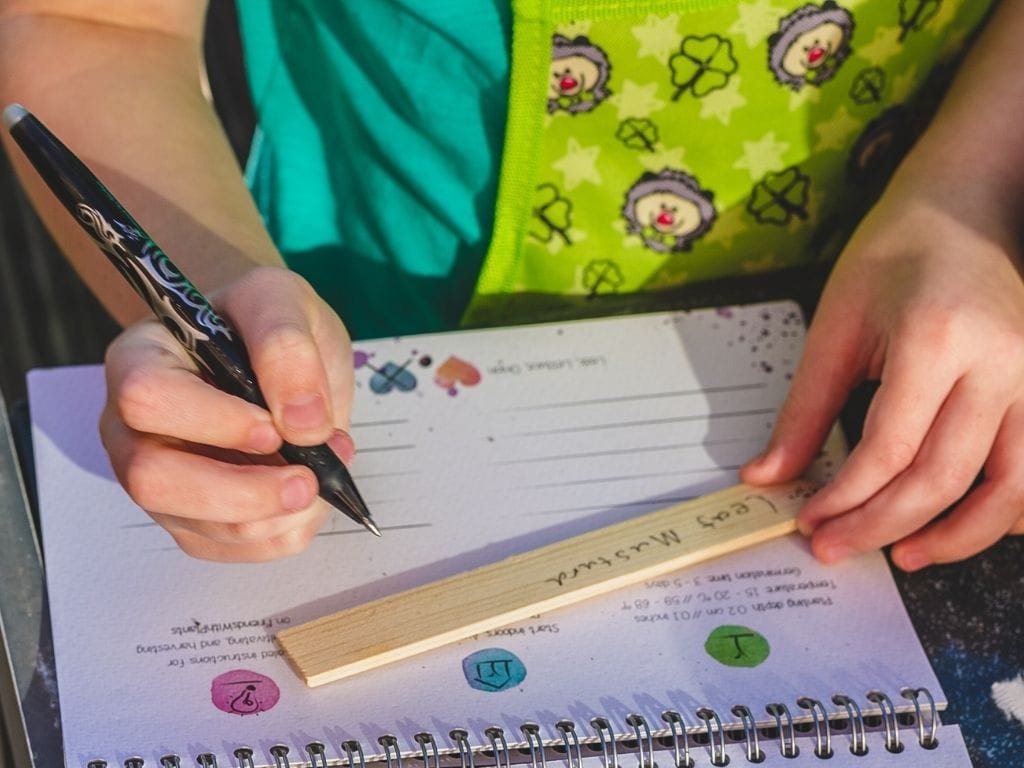 Girl writing on wooden marker to lable plants from the Growable Calendar