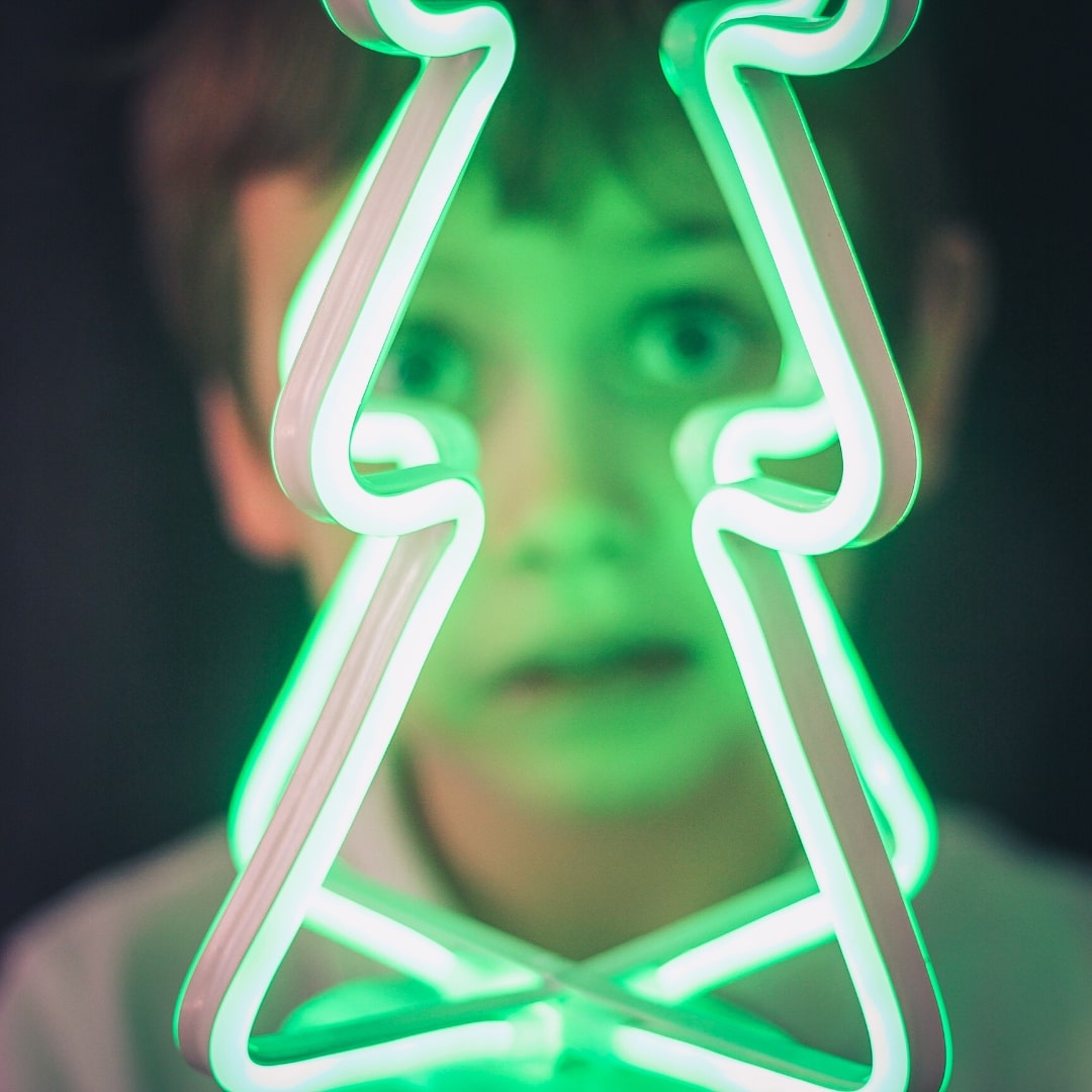 Face of a boy behind a green flourescent christmas tree lamp