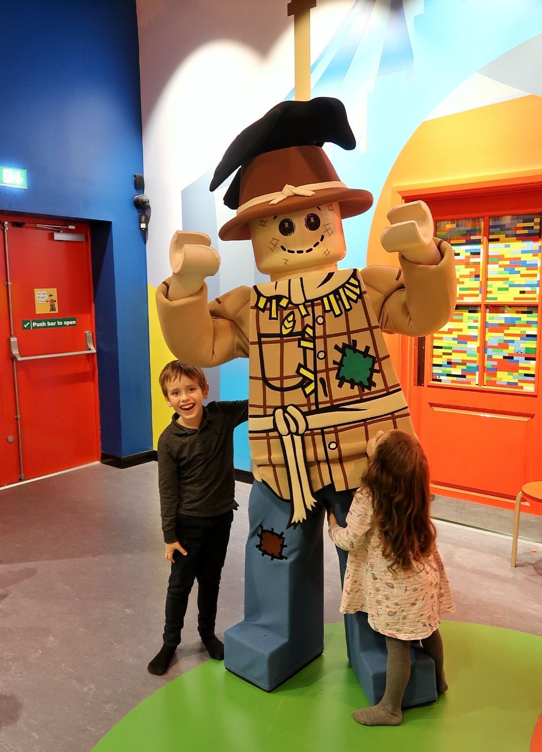 Boy and girl smiling in front of a person dressed as a lego character
