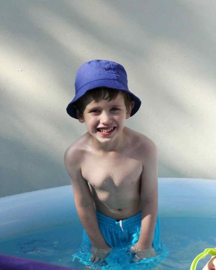 Boy smiling in a paddling pool with a blue hat
