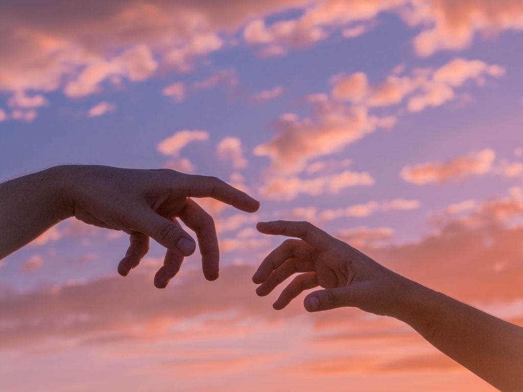 Two hands reaching for each other with a sunset behind